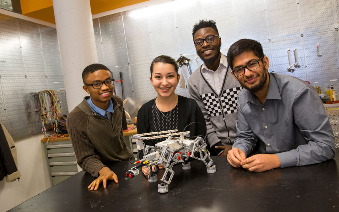 Four students pose with a robot.