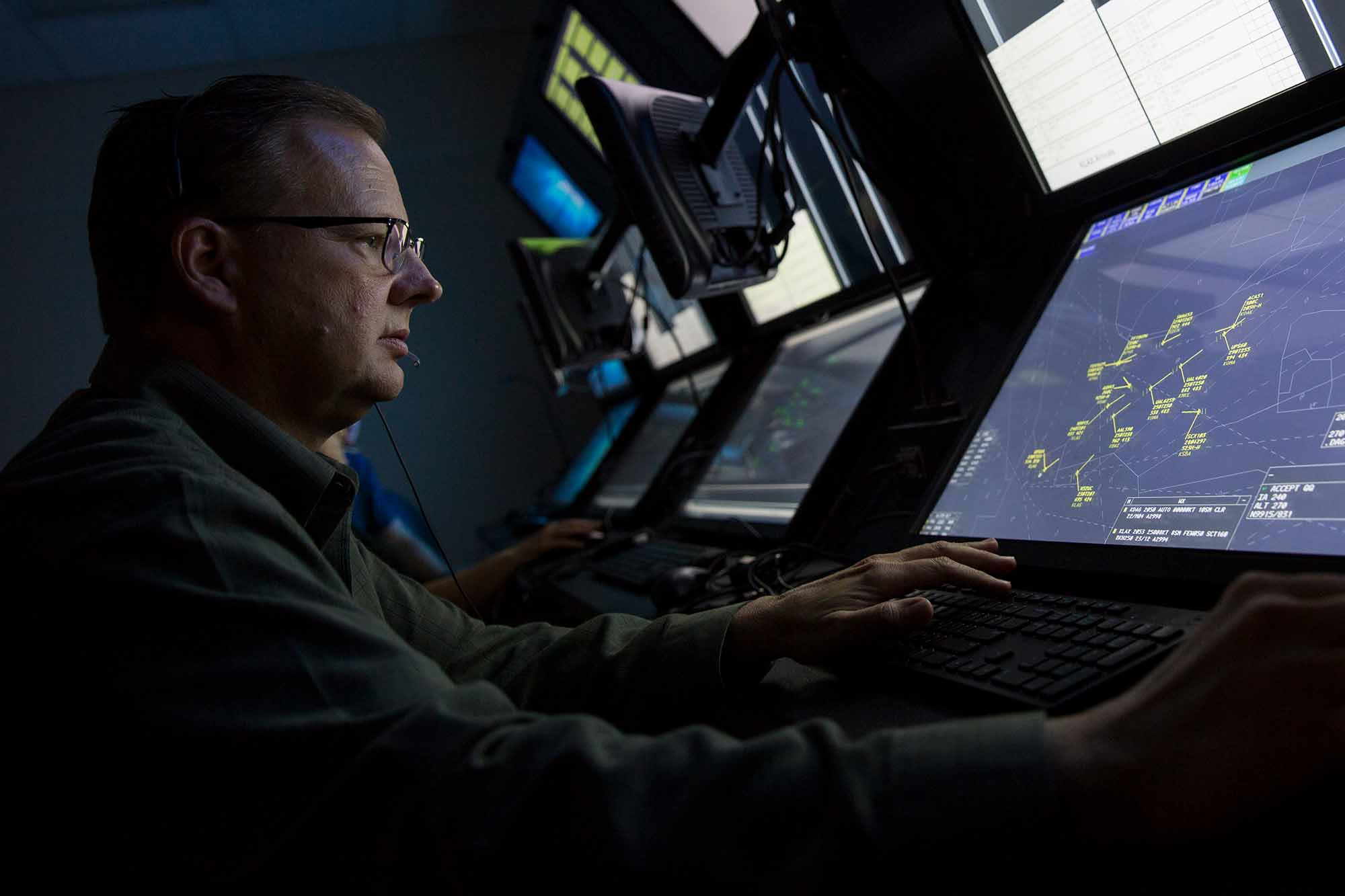 A man works at a station in a large array of computers and monitors used for air traffic control simulation.
