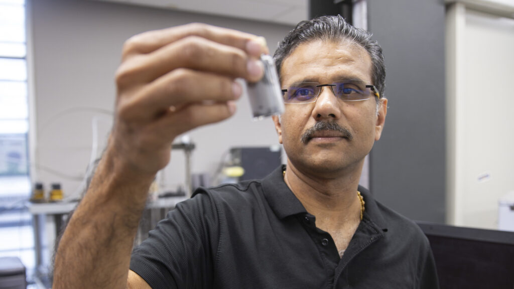 ASU professor Narayanan Neithalath holds a small concrete object in front of him, looking at it.