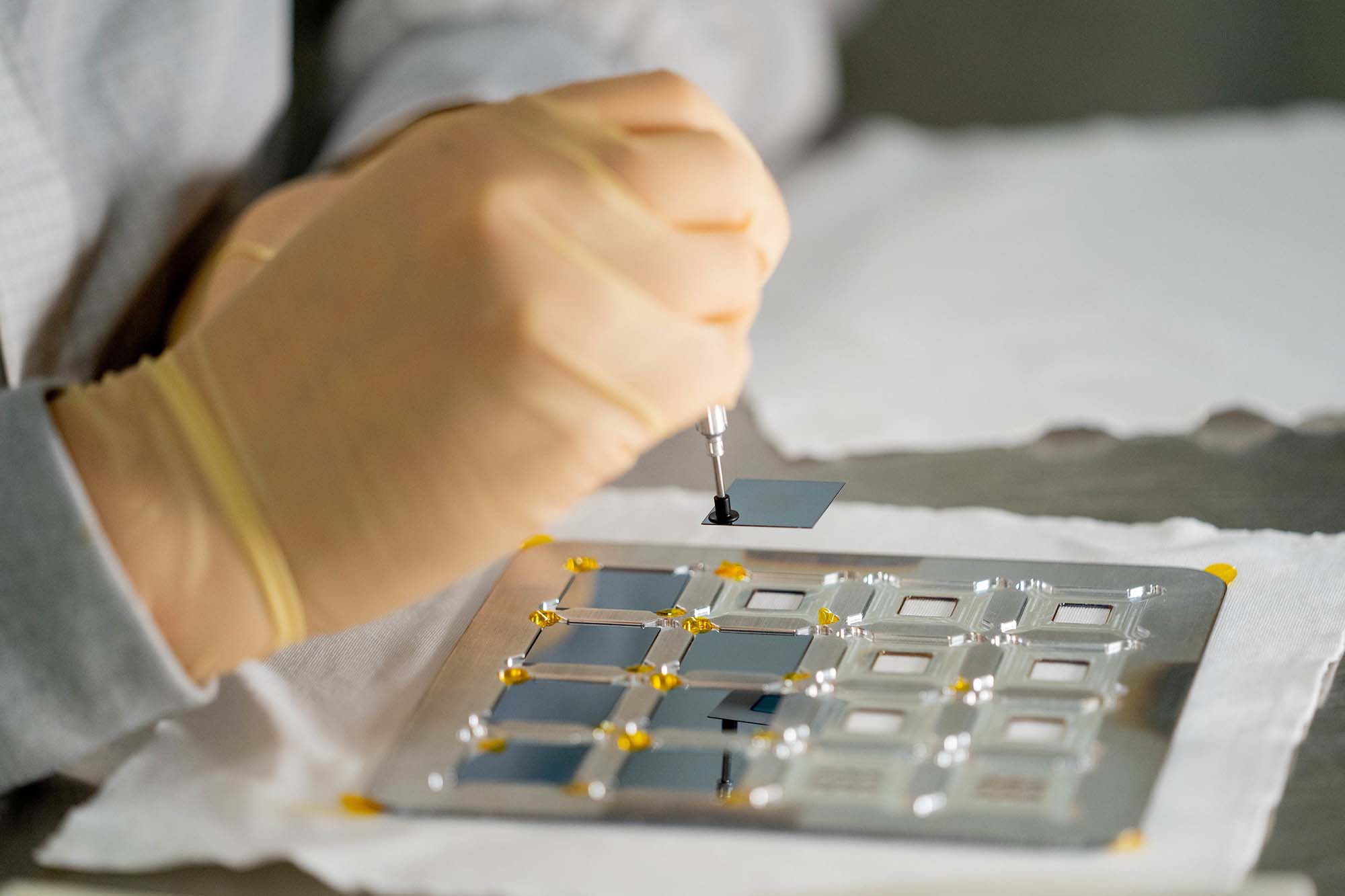 Close up of a researcher's gloved hands handling microelectronic parts in a clean room environment at ASU's MacroTechnology Works facility.