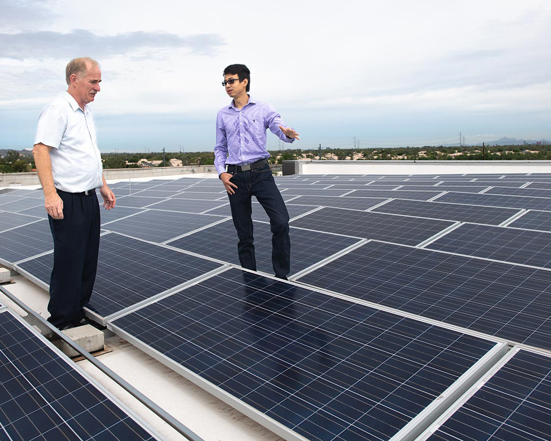 ASU researcher Jason Yu (right) talks with another man while they stand on an array of solar panels.