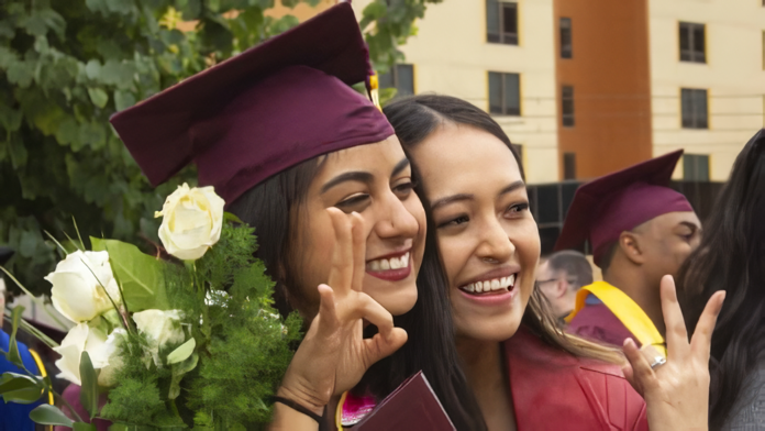 Two students pose with graduation caps on.