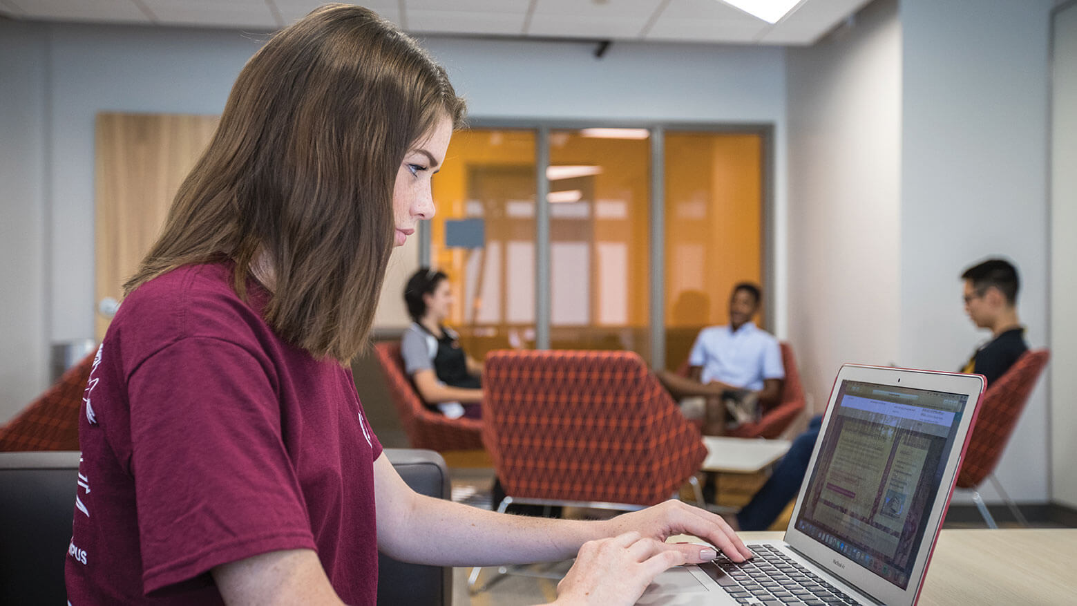 A student sits in a lounge area studying with an open laptop in front of her
