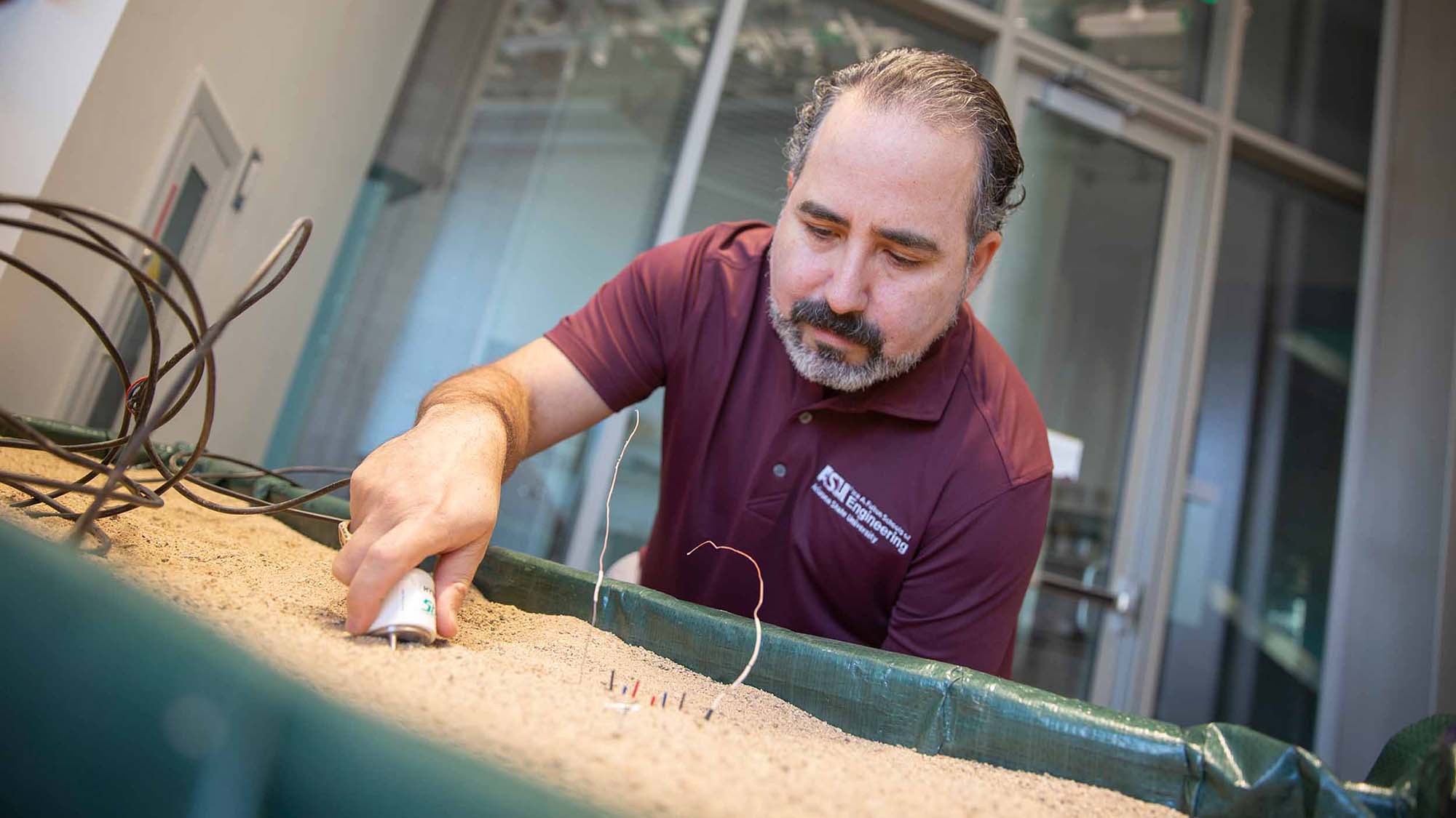 Enrique Vivoni holds an electronic sensor in a container of sand, measuring the water content.