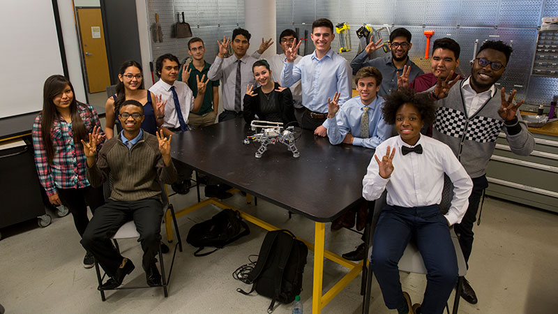 A bunch of students pose around a little dog-shaped robot