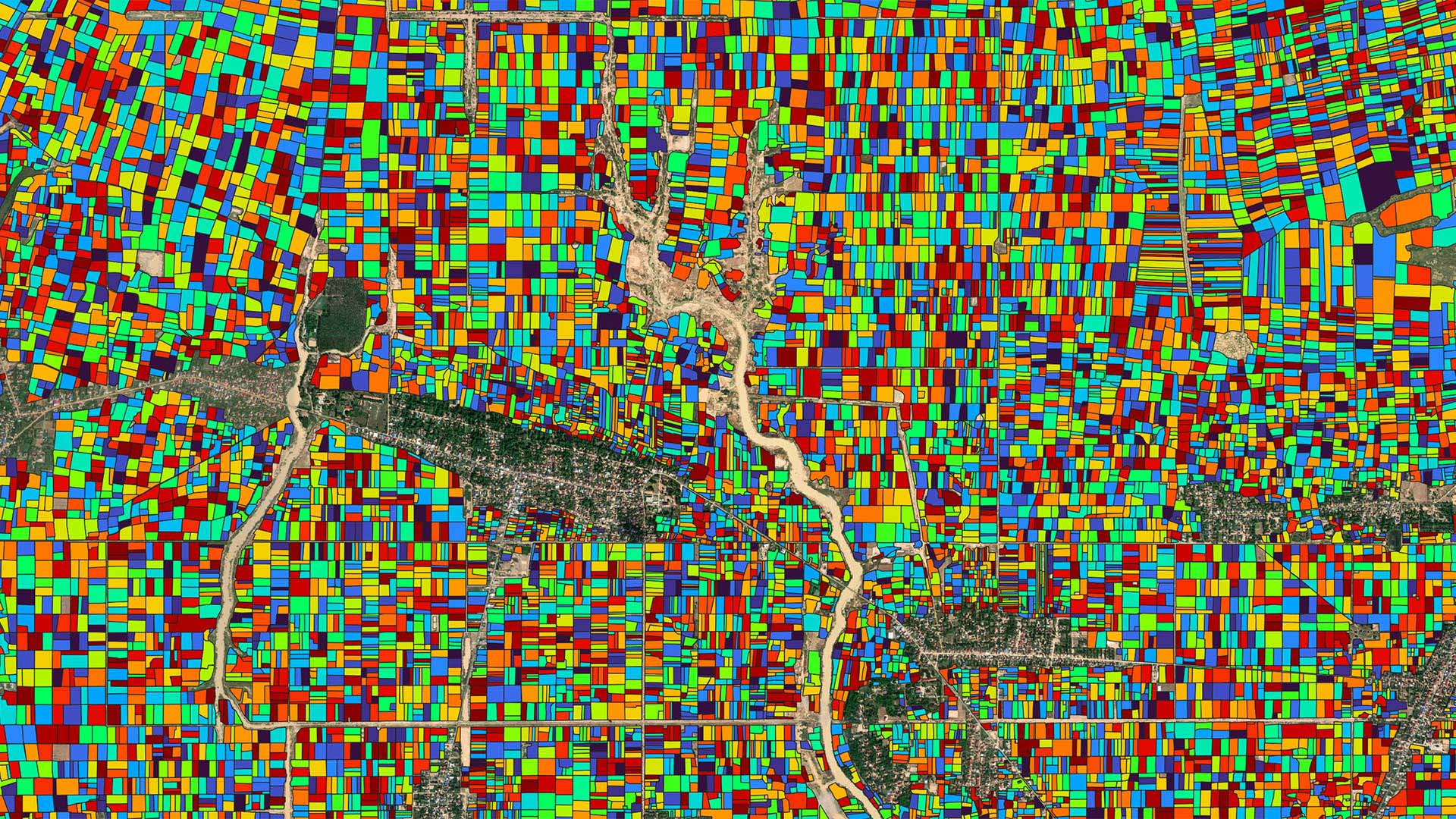 A satellite map overlaid with brightly colored geometric shapes representing individual agricultural fields in a rural region, used to visualize cropland boundaries.